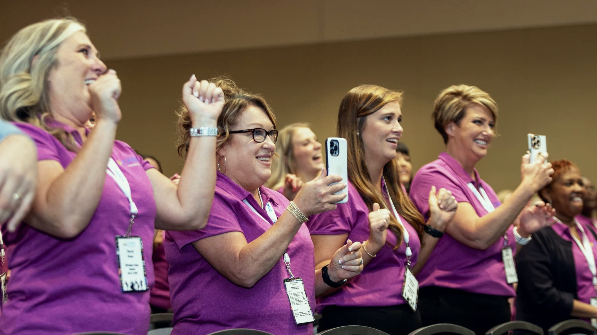 Conference attendees in matching shirts cheering and filming on their phones