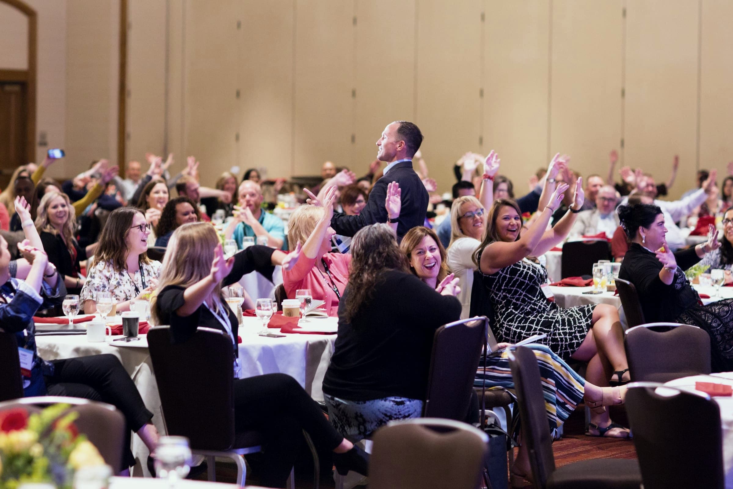 Kevin among the tables of a packed ballroom as audience members raise their hands