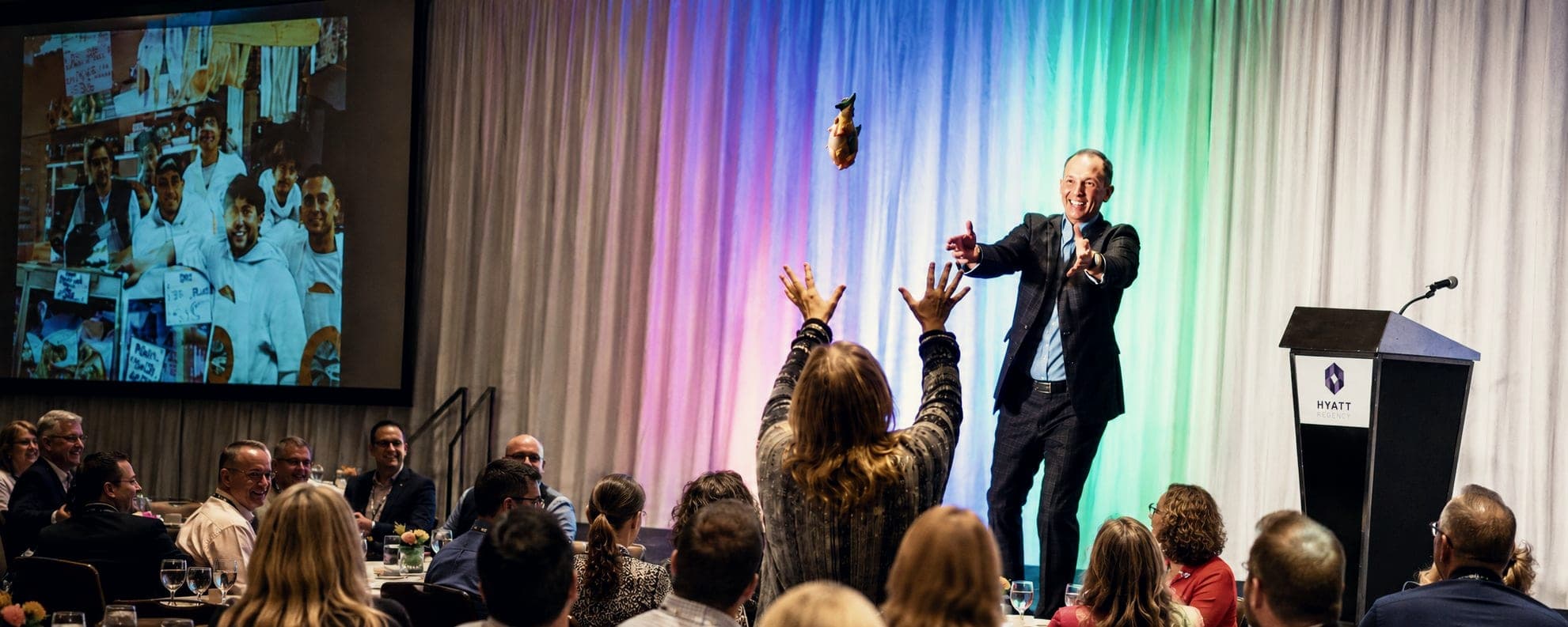Kevin speaking to a ballroom audience, arms raised
