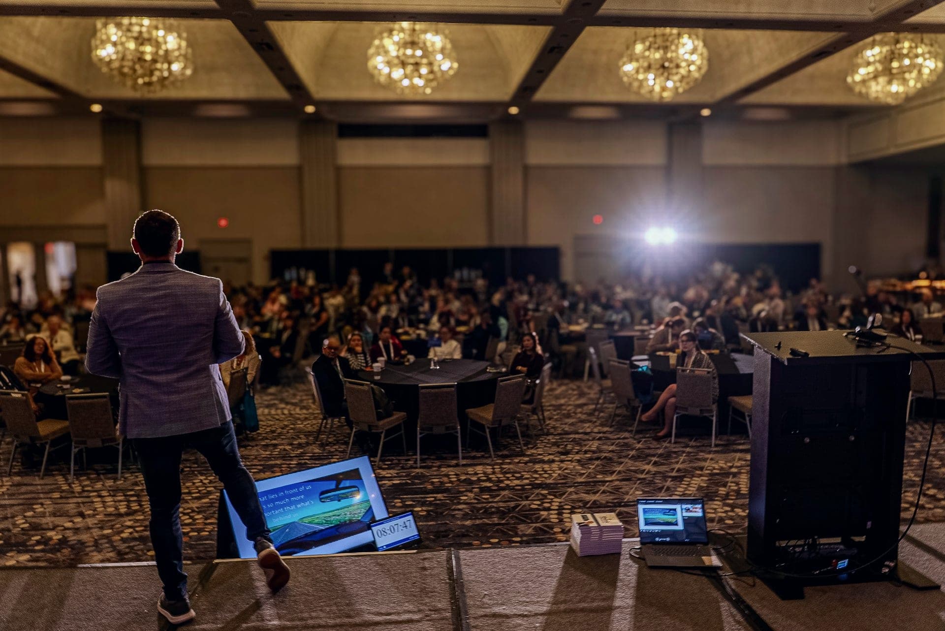 Kevin on stage, seen from behind, facing a full ballroom audience