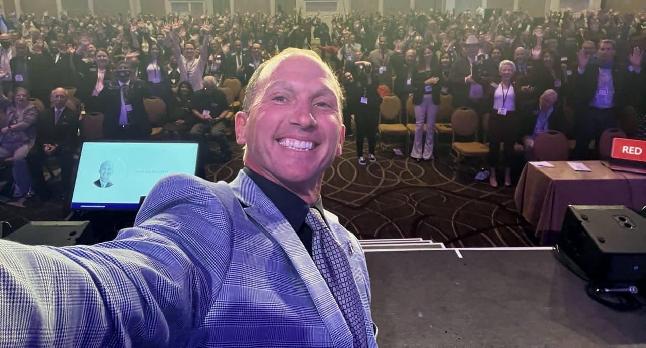 Kevin taking a selfie from the stage with a full ballroom audience behind him