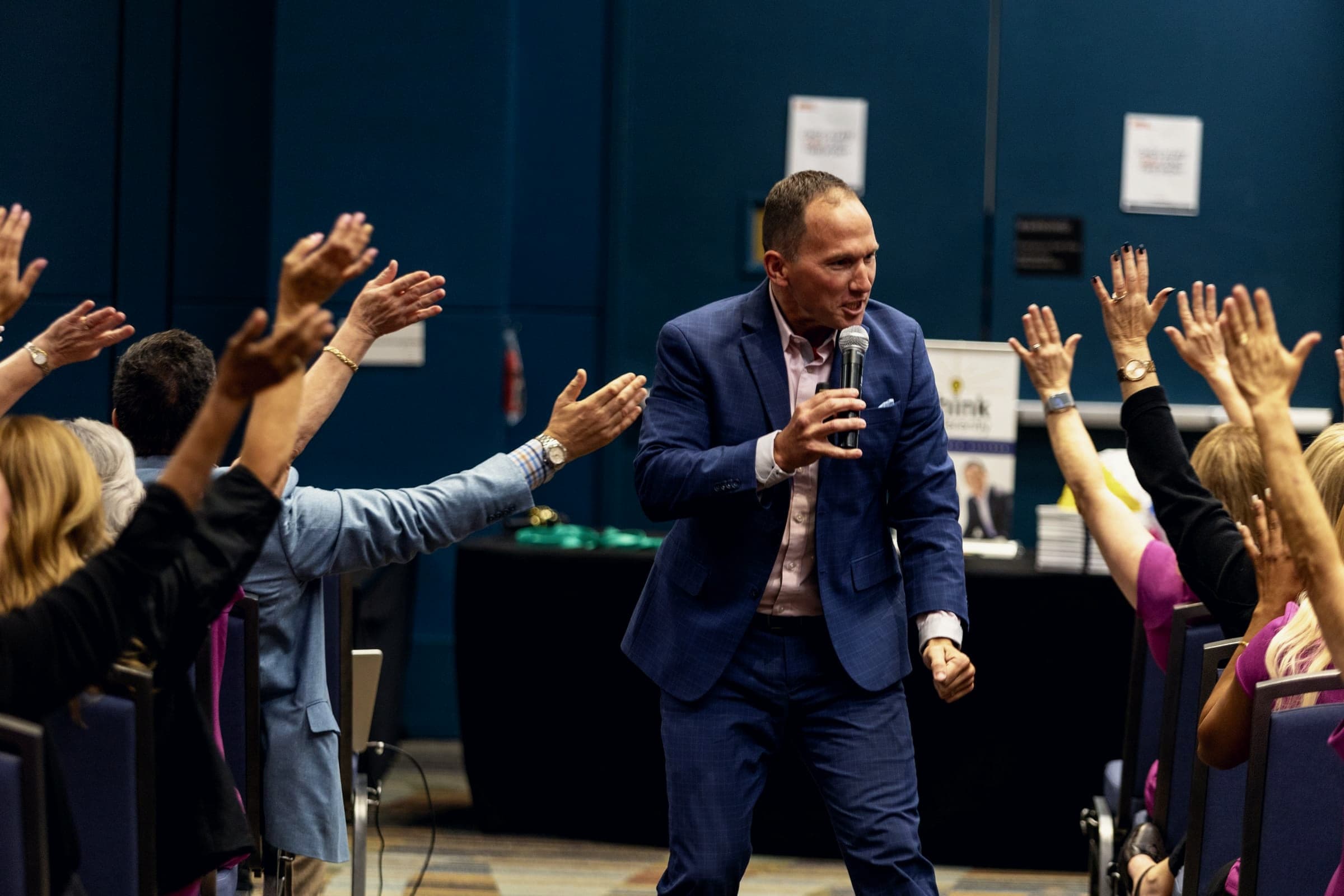 Kevin walking through a conference crowd with a microphone as attendees throw their hands up